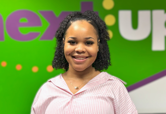 Alexis Stokes stands in front of the NextUp logo in their office