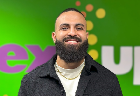 Amir Elsayed, the Director of Strategic Partnerships and Initiatives at NextUp, poses in front of the organization's logo in their office in Richmond, VA.