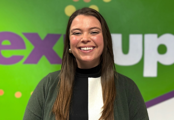 Annie Hedrick poses in front of the NextUp logo in the staff office located in Richmond, VA