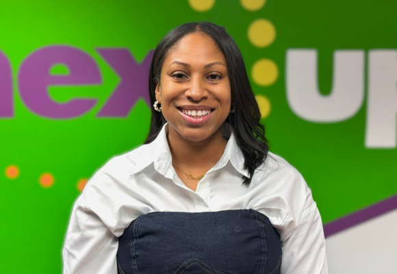 Dominique Menefee poses in front of the NextUp logo smiling