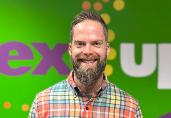 Eric Garmon, Director of Systems Data and Analytics, smiles in front of the NextUp logo.