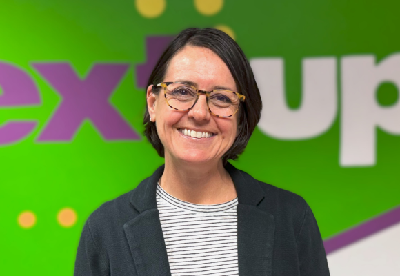 Abby Ritt poses in front of the NextUp logo in their office